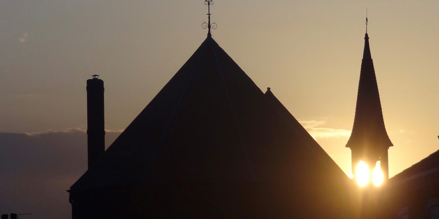 A silhouette shot of a church, with the setting sun visible through its steeple