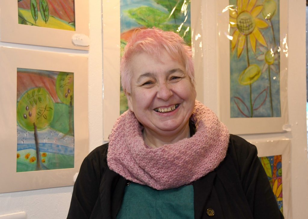 Mary Passeri stands smiling in front of some of her paintings