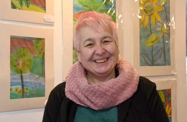 Mary Passeri stands smiling in front of some of her paintings