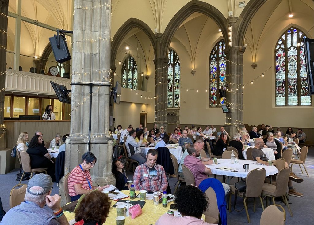 A church building full of people sitting round tables, at the Dignity For All conference in Leeds in June 2023