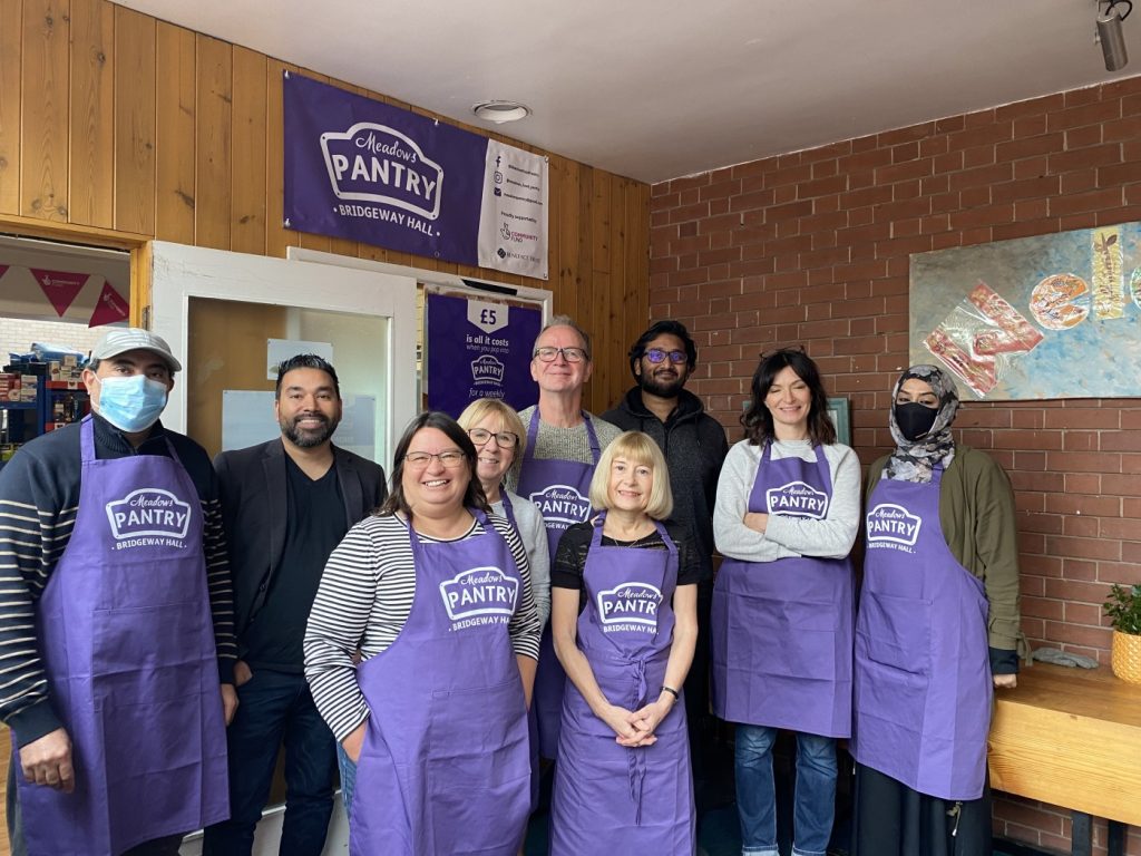 A group shot of 9 people inside Nottingham's first Your Local Pantry. Most are in purple aprons; one is holding a basket of food.