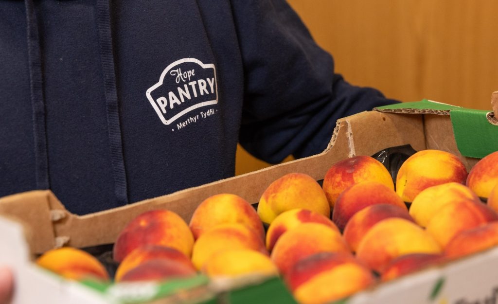 A volunteer in a Pantry hoody carries a crate of peaches