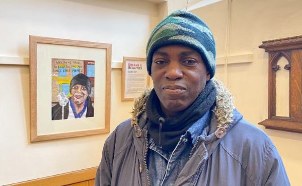 Wayne stands in front of his portrait