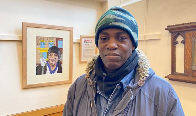 Wayne stands in front of his portrait