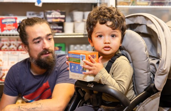 A toddler in a pushchair holds a box of rice, at a Your Local Pantry