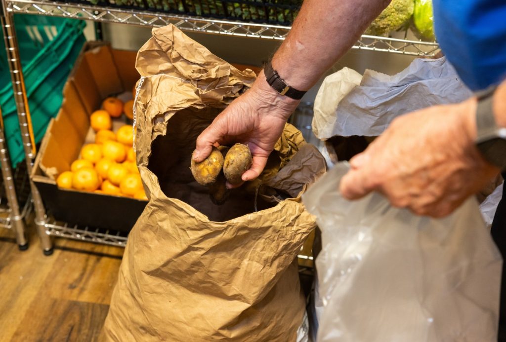 A volunteer lifts potatoes from a sack. Only his hands are shown, his face is off-camera.