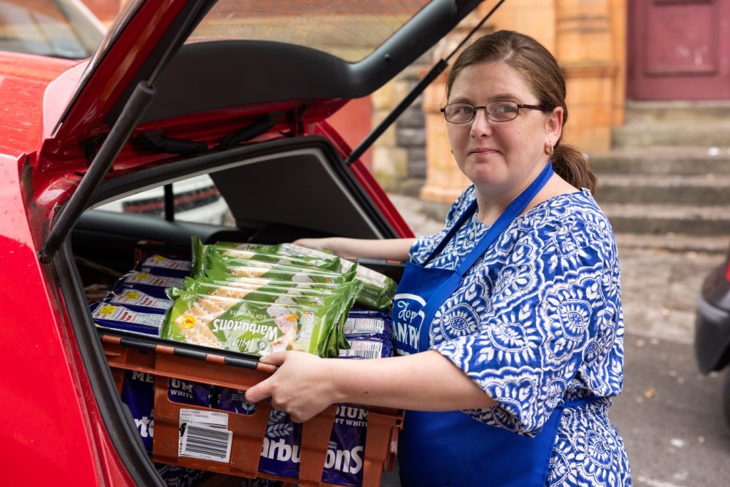 A volunteer lifts a crate of bread out of a car boot.