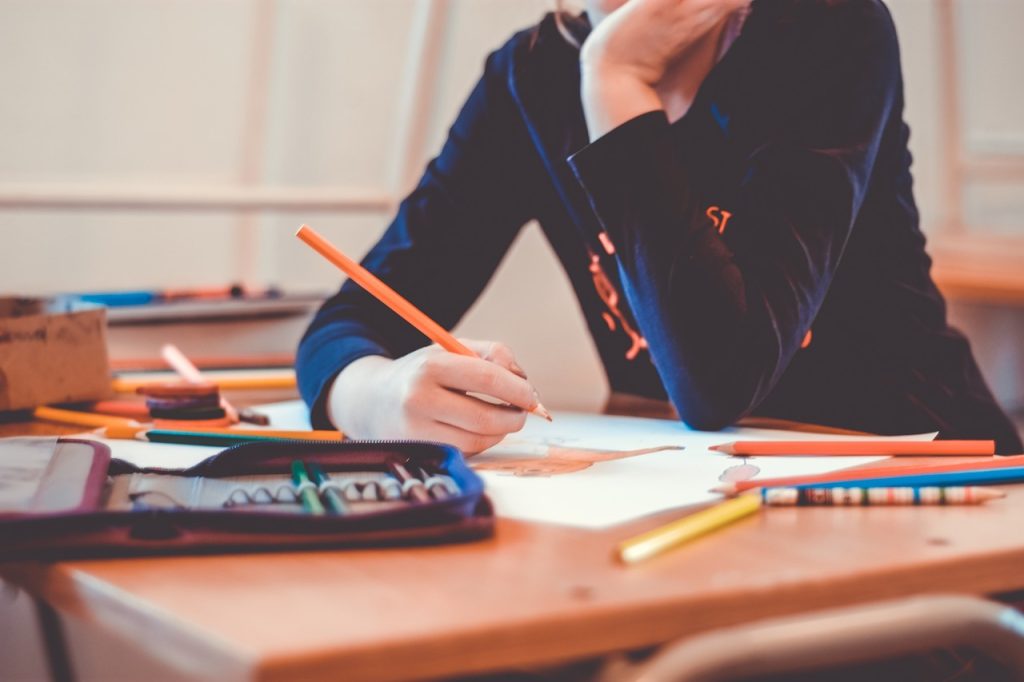 A stock posed image of a pupil in a classroom, writing at a desk.