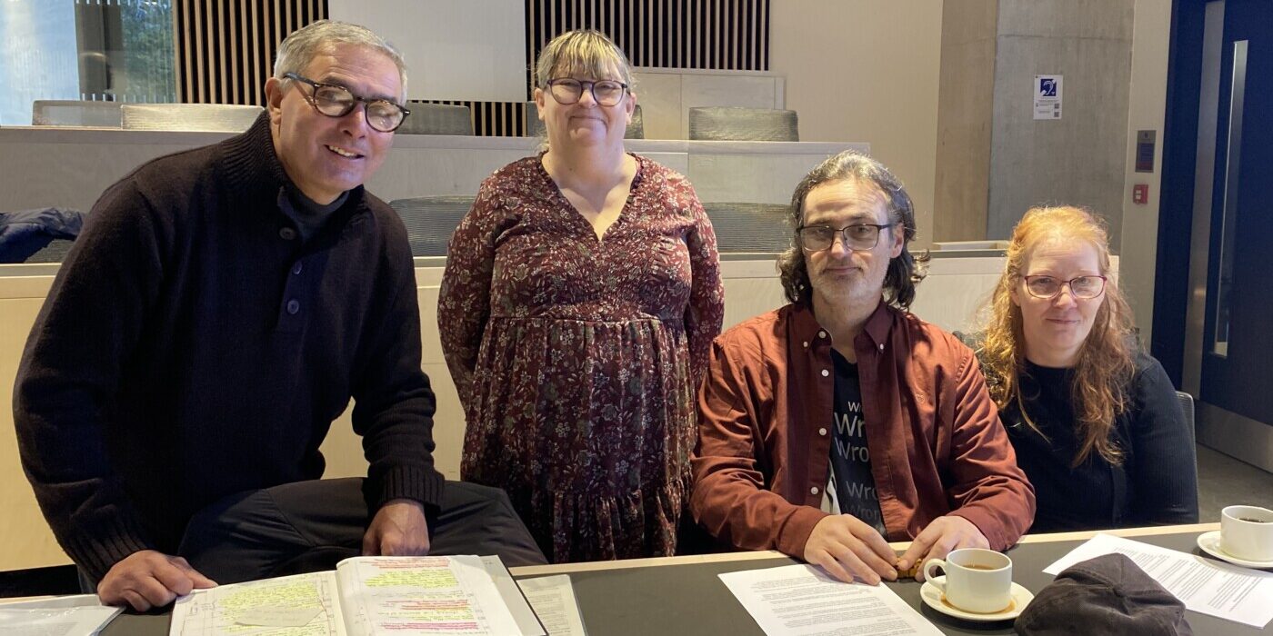 Four people behind a desk, looking at the camera. Two are standing; two sitting.