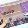 A hand holding a bundle of Spark newsletters