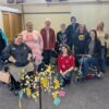 A group of people in a church hall, facing the camera, beside an artificial tree decorated with paper mesages.