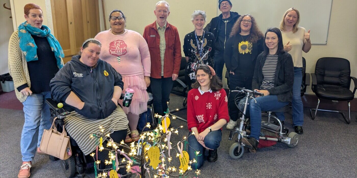 A group of people in a church hall, facing the camera, beside an artificial tree decorated with paper mesages.