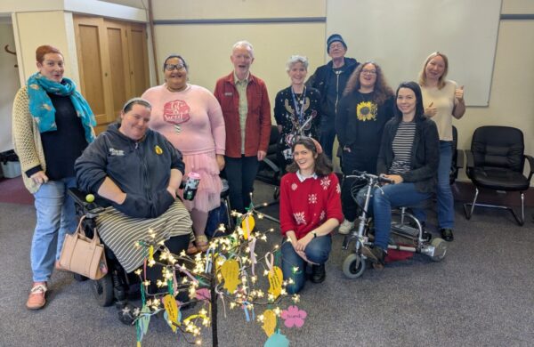 A group of people in a church hall, facing the camera, beside an artificial tree decorated with paper mesages.