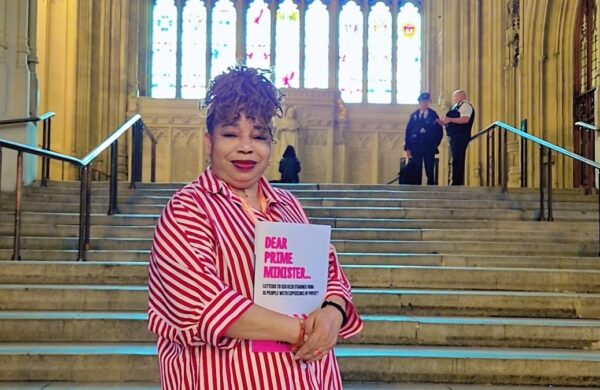 Glory holding the "Dear Prime Minister" booklet, standing on a staircase in the Houses of Parliament.