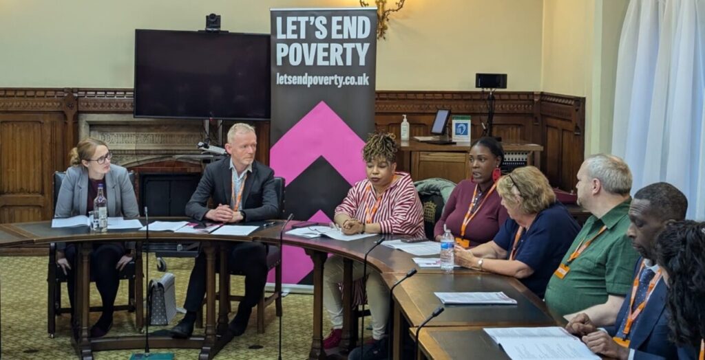 People sitting at a curved line of desks, in front of a Let's End Poverty banner