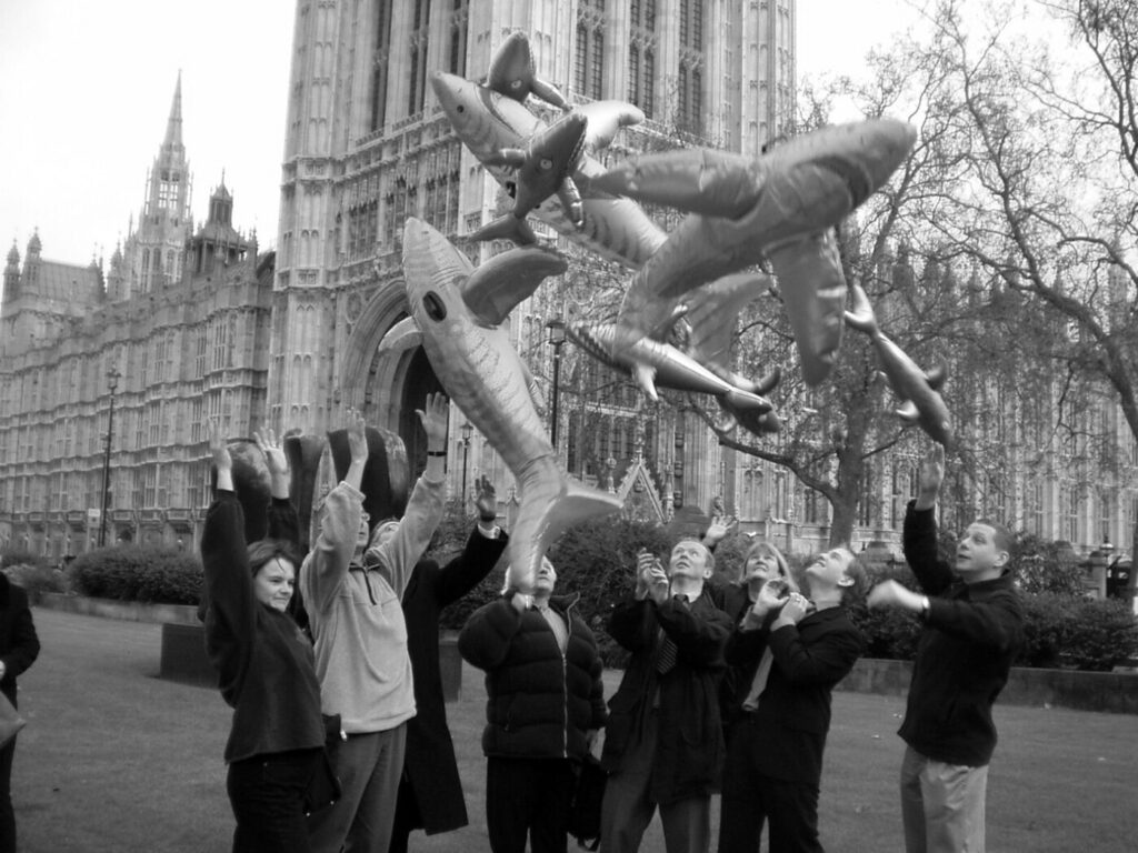 A black and white photo of inflatable sharks being thrown in the air, outside Parliament